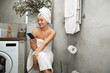 cheerful young caucasian woman in a towel sitting in the toilet with a mobile phone 
