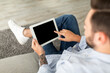 © Prostock-studio - Young man using digital tablet with blank black screen, browsing website or showing new app, sitting on sofa at home