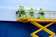 yellow self propelled scissor lift with workers against a blue sandwich panel wall background