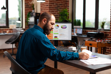 Entrepreneur man sitting at desk table analyzing business documents working at marketing presentation planning company strategy in startup office. Businessman looking at management paperwork