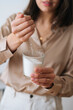 © dikushin - Vertical cropped shot of female artisan pouring dry mixture by hand into measuring transparent glass for creating candle building mixture. Process of making handmade natural candle at workshop.