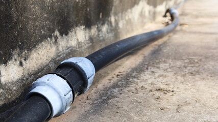 Old HDPE Straight Coupling. Compression fitting straight coupling connects to black plumbing pipe beside concrete wall with copy space. selective focus