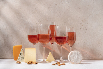 Set of rosé wine in glasses on tablecloth covered table with variety of cheeses. Romantic party, vacation, holiday concept