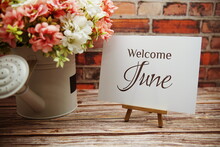 Welcome June Text With Flower Bouquet Decoration On Wooden And Old Brick Wall Background