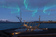 Reykjavik, Iceland. 12.22.2021. Reykjavik's Symbol, The "Sun Voyager" Steel Sculpture Against The Backdrop Of The City At Night, Snow-capped Mountains And The Northern Lights