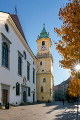 Bratislava town hall tower with Jesuit church and sun flare in yellow autumn leaves