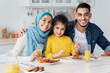 © Prostock-studio - Happy Muslim Family Posing At Camera While Eating Breakfast In Kitchen