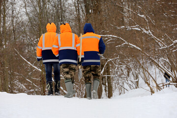 Wall Mural - Three workers in orange uniform with a shovels going to clean up the snow in park. Street cleaning in winter city