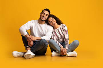 Wall Mural - Romantic young middle eastern couple sitting on floor over yellow background