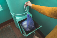 A Woman's Hand With A Garbage Bag Opens The Hatch Of The Garbage Chute And Throws Garbage There. Selective Focus