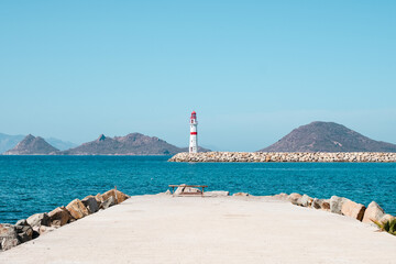 Wall Mural - Lighthouse standing at the coast of Bodrum, Turkey. Red white lighthouse with islands on turquoise sea.