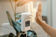 © JinnaritT - Customer raised hand at digital thermometer with temperature scanning machine for fever before entering area. Screening to prevent infected people from entering restricted areas. Covid-19 concept.