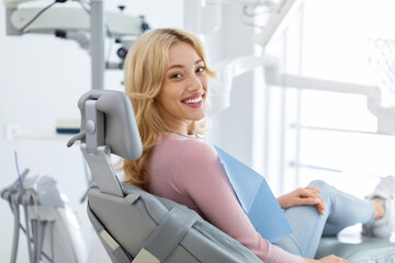 Smiling and relaxed young woman sitting at dental chair