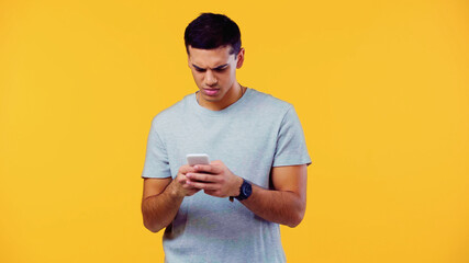 sad young man in t-shirt messaging mobile phone isolated on yellow.