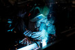 © Tetiana - An experienced worker in a dark workshop welds metal for billets.
