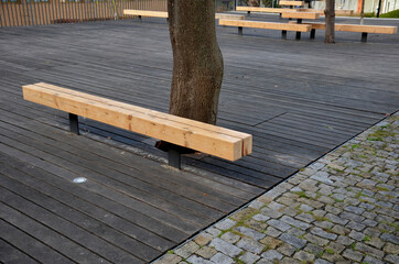 massive bench in the park under a tree in the park urban style beam shape on metal legs in the square. grass grate made of metal and concrete striped tile design with holes for soil grass turf, trunk