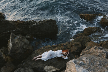 Poster - Barefoot woman in a white dress lying on a stone in a white dress view from above