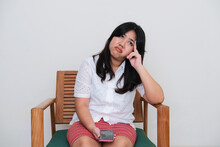 Adult Asian women sitting on the chair showing boring expression while holding mobile phone