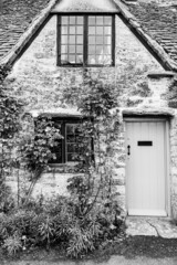 Wall Mural - Facade of traditional small cottage home in Bibury village, Cotswolds, Egland, UK. Rurar house with wooden door and rose bushes