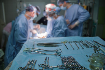 Wall Mural - Closeup of surgical tools on table and team of surgery doctors operating a patient in hospital room