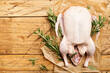 Raw whole duck, pepper and rosemary. Wooden background. Top view. Copy space