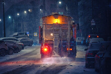 Salt Spreading. Snow Plow Service Truck Removing Snow And Spreading Salt On Snowy City Road During Blizzard, Night Work Road Maintenance. Truck Spreading De-icing Salt On Snowy And Icy Asphalt Road