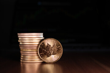 a maple leaf gold coin stands in front of a stack of gold coins