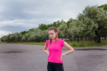 Portrait of young smiling woman in sportswear and wireless earphones getting ready for outdoors running or physical training.