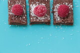 Fototapeta  - Raspberry and coconut zest on three pieces of chocolate cake. Blue background. Top view. Brownie
