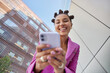 © wayhome.studio  - Positive fashionable woman uses mobile phone for chatting sends text messages surfs social networks dressed in pink jacket poses against urban background strolls in city has trendy hairstyle