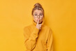 © WHstudio Leushin N - Beautiful fair haired young woman makes silence gesture asks to be mute and not spread rumors wears sweater and eyeglasses isolated over vivid yellow background. Hush dont make any sound please