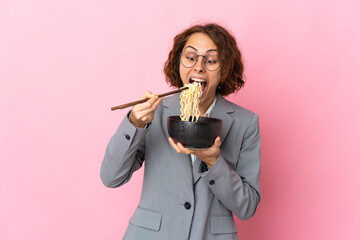 Young English woman isolated on pink background holding a bowl of noodles with chopsticks and eating it