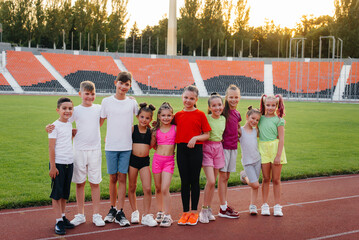 Wall Mural - A large group of children, boys and girls, rejoice together and wave their hands at the stadium during the sunset post game. A healthy lifestyle.