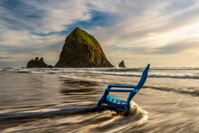 Blue Chair In Flowing Surf At Cannon Beach, Oregon With Haystack Rock In The Background