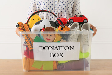 Wall Mural - Woman holding donation box with child goods against light background, closeup