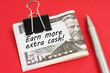 On a red background lies a pen and dollars clamped with a clip with the inscription on paper - Earn more extra cash