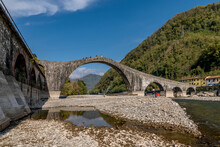 People Walk On The Almost Dry Serchio River Bed Under The Ponte Della Maddalena, Lucca, Italy