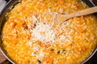 Cooking risotto with pumpkin in a pan - adding grated cheese to the dish, close-up