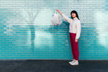 Young Woman Showing Mesh Bag With Empty Plastic Bottles Standing By Turquoise Brick Wall
