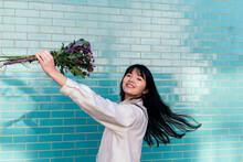Cheerful Woman Holding Bouquet Dancing By Turquoise Brick Wall