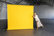© Westend61 - Businesswoman pointing at blank yellow backdrop