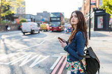 Woman With Smart Phone Waiting At Roadside In City