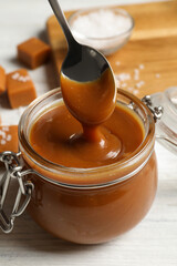 Wall Mural - Taking yummy salted caramel with spoon from glass jar at white wooden table, closeup