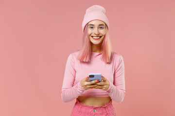 Young happy woman with bright dyed rose hair in rosy top shirt hat hold in hand use mobile cell phone isolated on plain light pastel pink background studio portrait. People lifestyle fashion concept