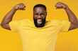 © ViDi Studio - Young overjoyed happy black man 20s wearing bright casual t-shirt showing biceps muscles on hand demonstrating strength power isolated on plain yellow color background studio People lifestyle concept