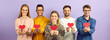 © Studio Romantic - Studio group portrait of happy cheerful positive kind mixed race multiethnic young people who celebrate Valentine's Day holding red paper hearts and smiling isolated on purple color banner background