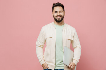 Wall Mural - Young smiling happy cheerful caucasian man 20s wearing trendy jacket shirt hold use closed laptop pc computer isolated on plain pastel light pink background studio portrait. People lifestyle concept.