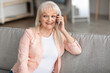 © Prostock-studio - Smiling mature woman talking on phone sitting on couch