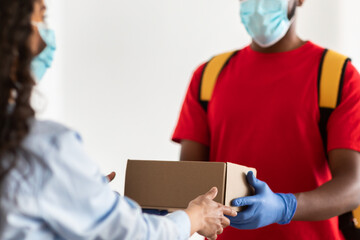 Black delivery man in mask giving cardboard box to client