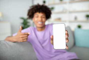 Wall Mural - Positive African American adolescent pointing at smartphone with mockup for mobile app on screen, selective focus